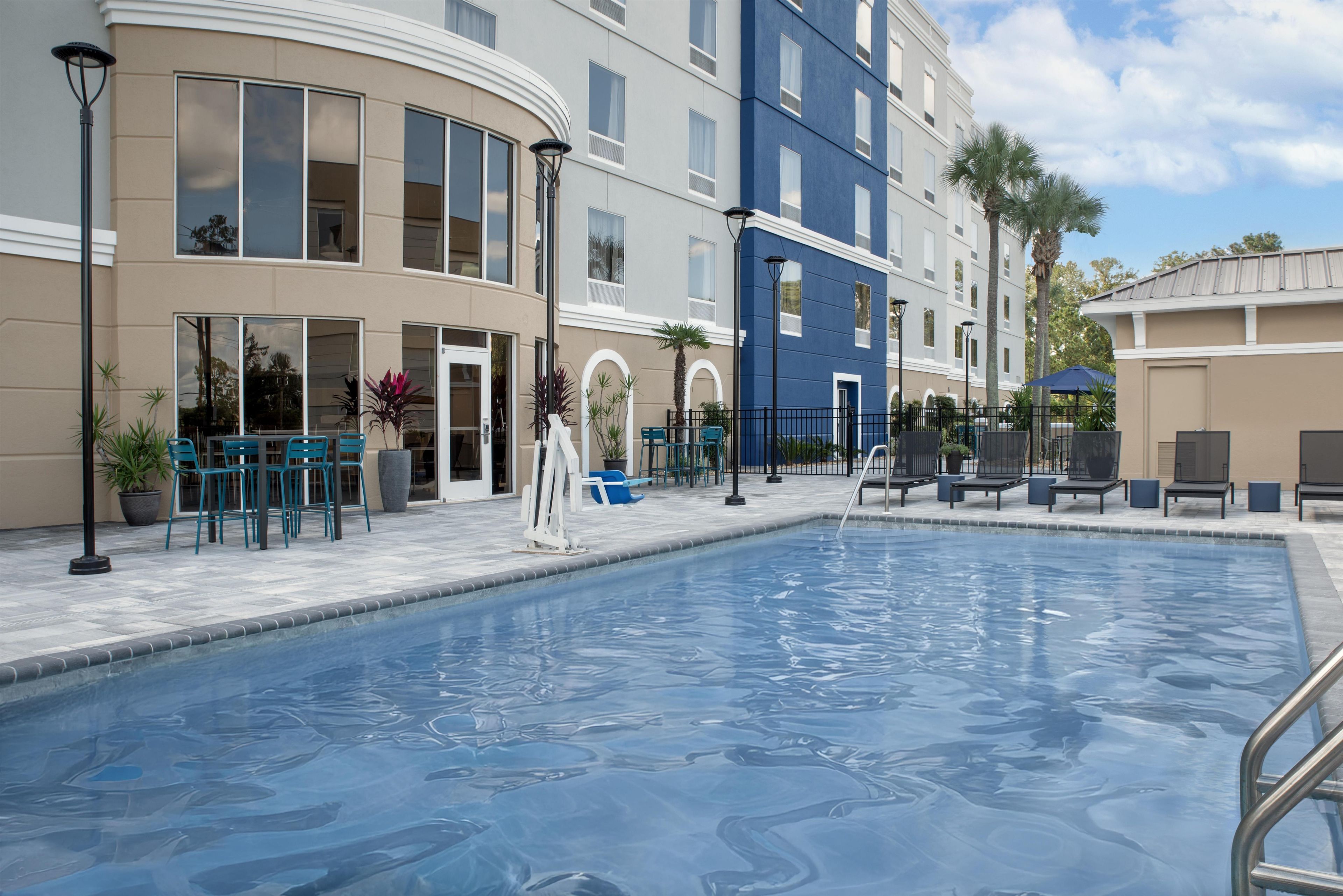 A swimming pool with a clear blue water surface, surrounded by lounge chairs and potted plants.