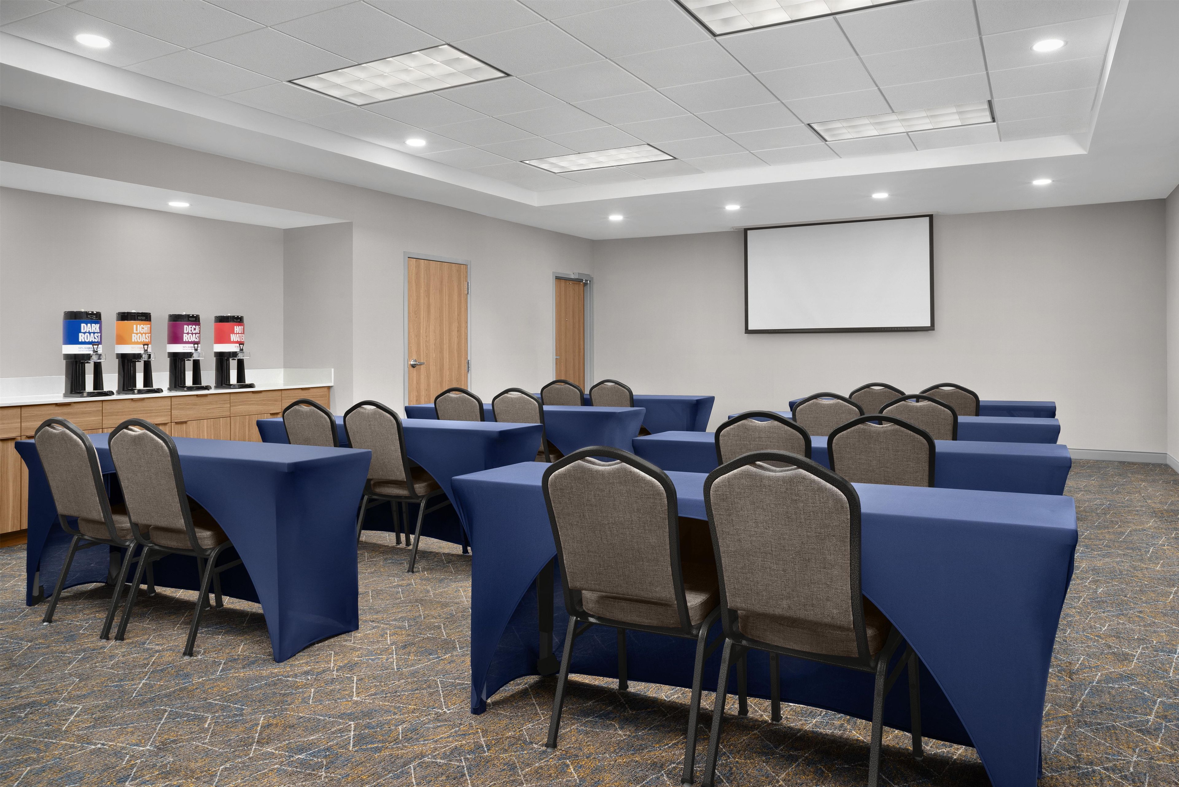A conference room with tables, chairs, a projector screen, and a coffee station.