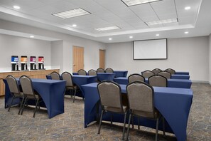 Una sala de conferencias con mesas, sillas, una pantalla de proyector y una zona de café.