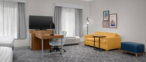 Habitación de hotel con una cama, un escritorio con computadora, un sofá, una mesita y un televisor.