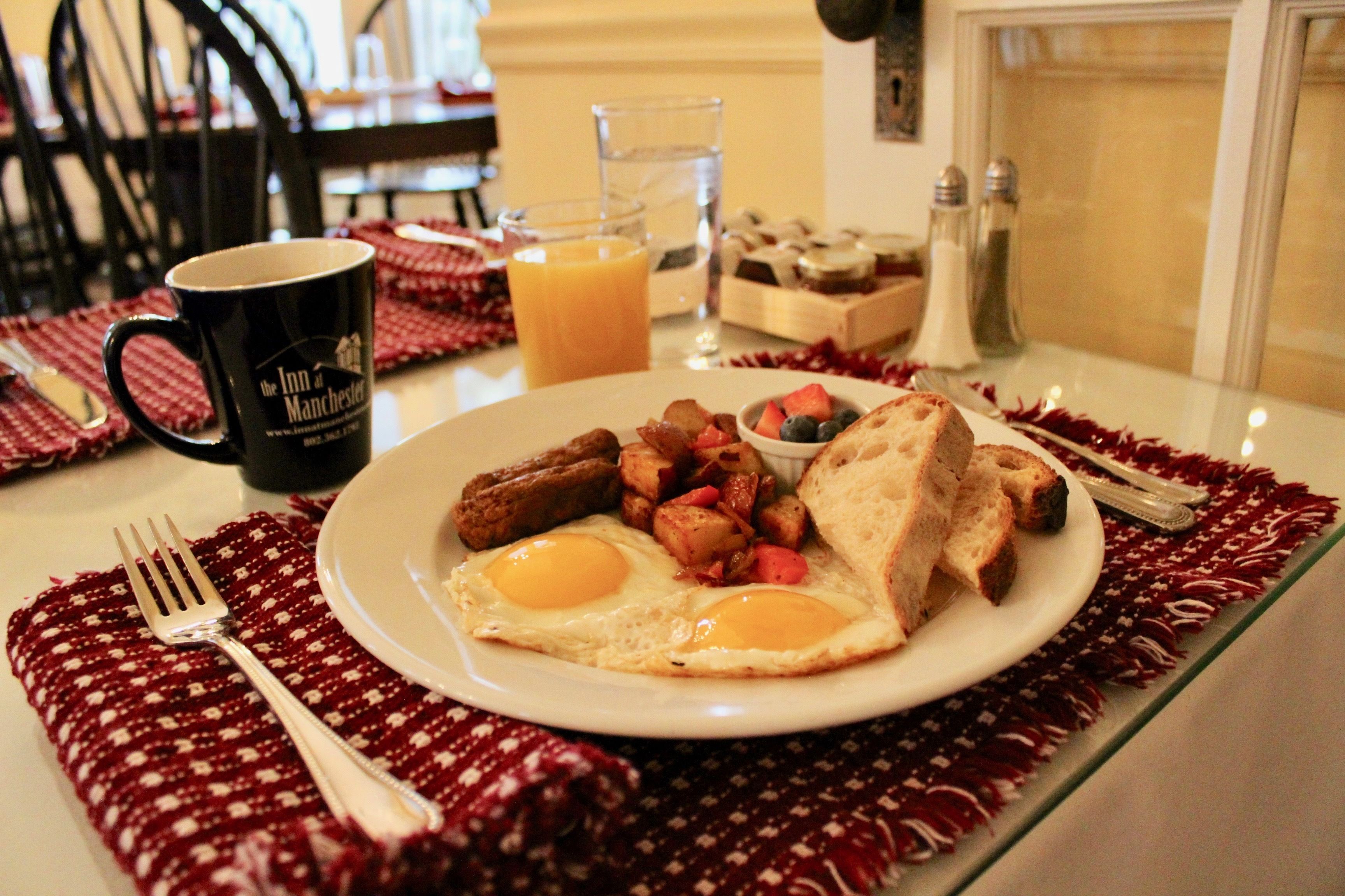A breakfast plate with eggs, toast, and potatoes, a mug, and a glass of orange juice on a table with a red placemat.