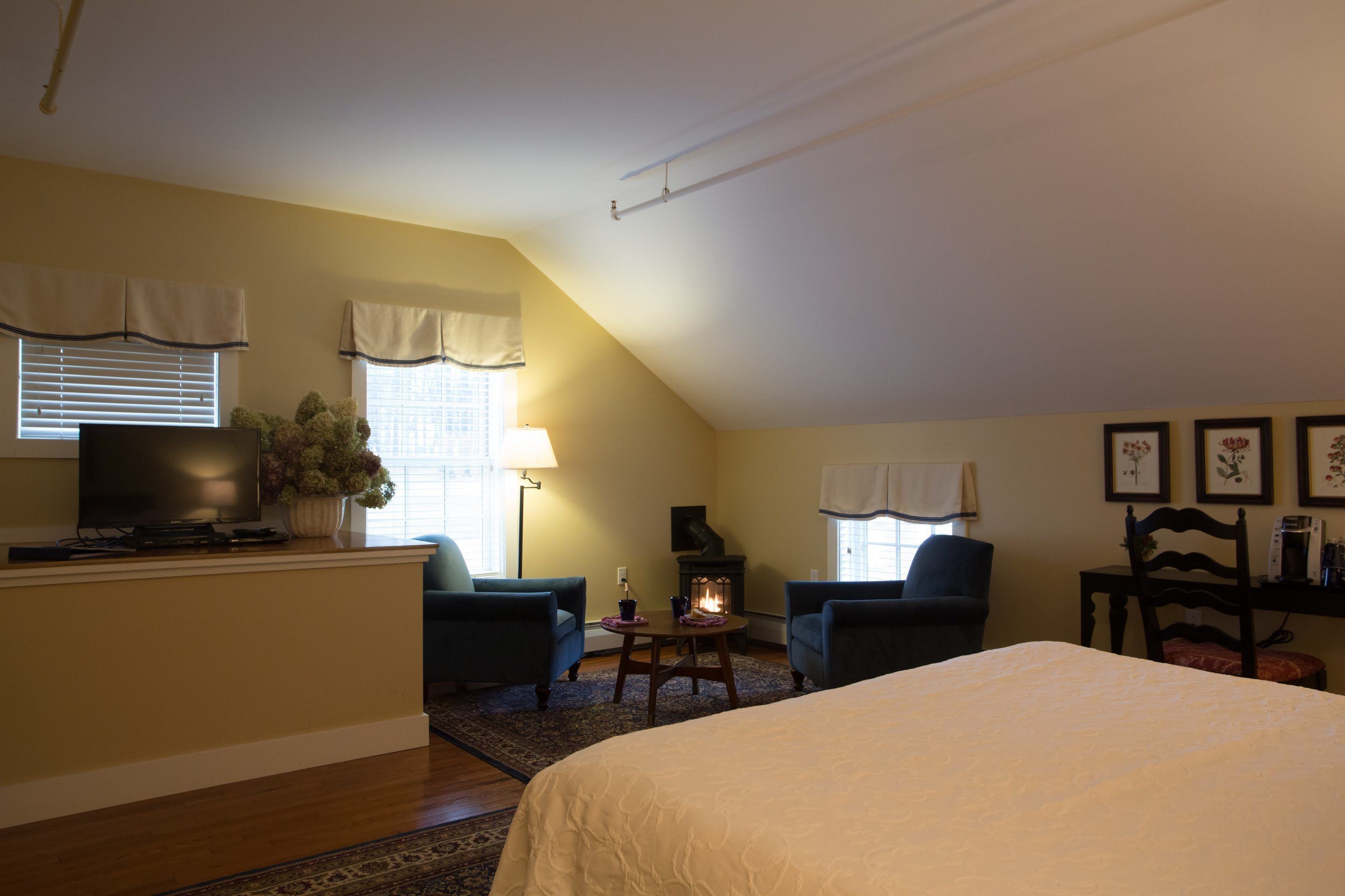 A cozy room with a bed, two armchairs, a small table, a fireplace, and a television.