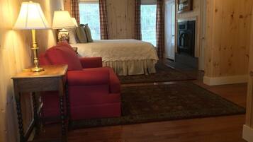 A cozy bedroom with a bed, a red armchair, a wooden nightstand with a lamp, and a fireplace.