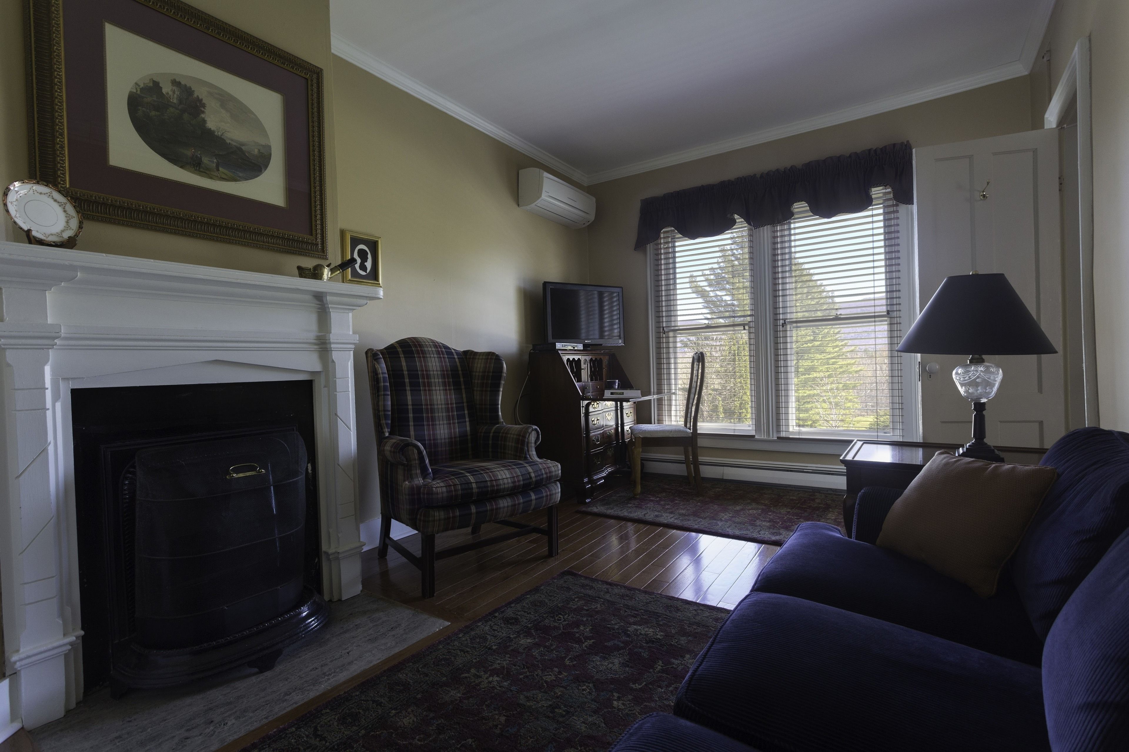A living room with a fireplace, a plaid armchair, a blue sofa, and a television on a stand.