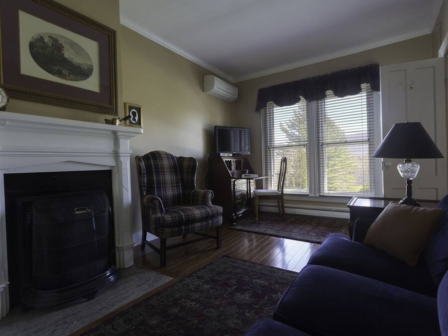 A living room with a fireplace, a plaid armchair, a blue sofa, and a television on a stand.
