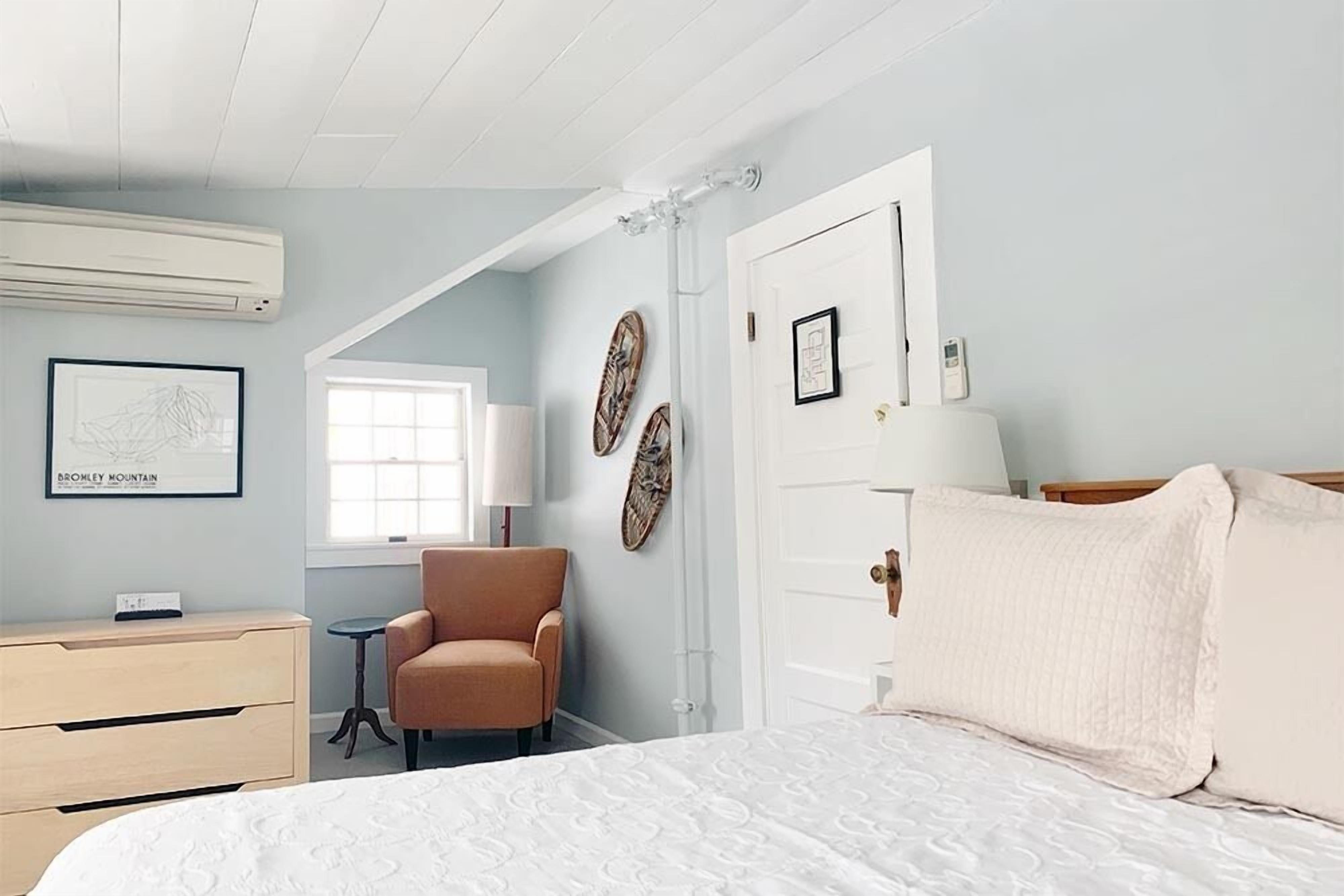 Un dormitorio con una cama, una silla, un aparador y una ventana.