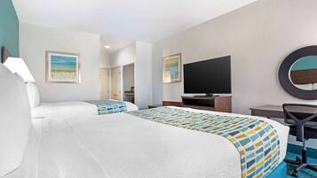 Habitación de hotel con dos camas, un escritorio, una silla, un televisor y obras de arte en las paredes.
