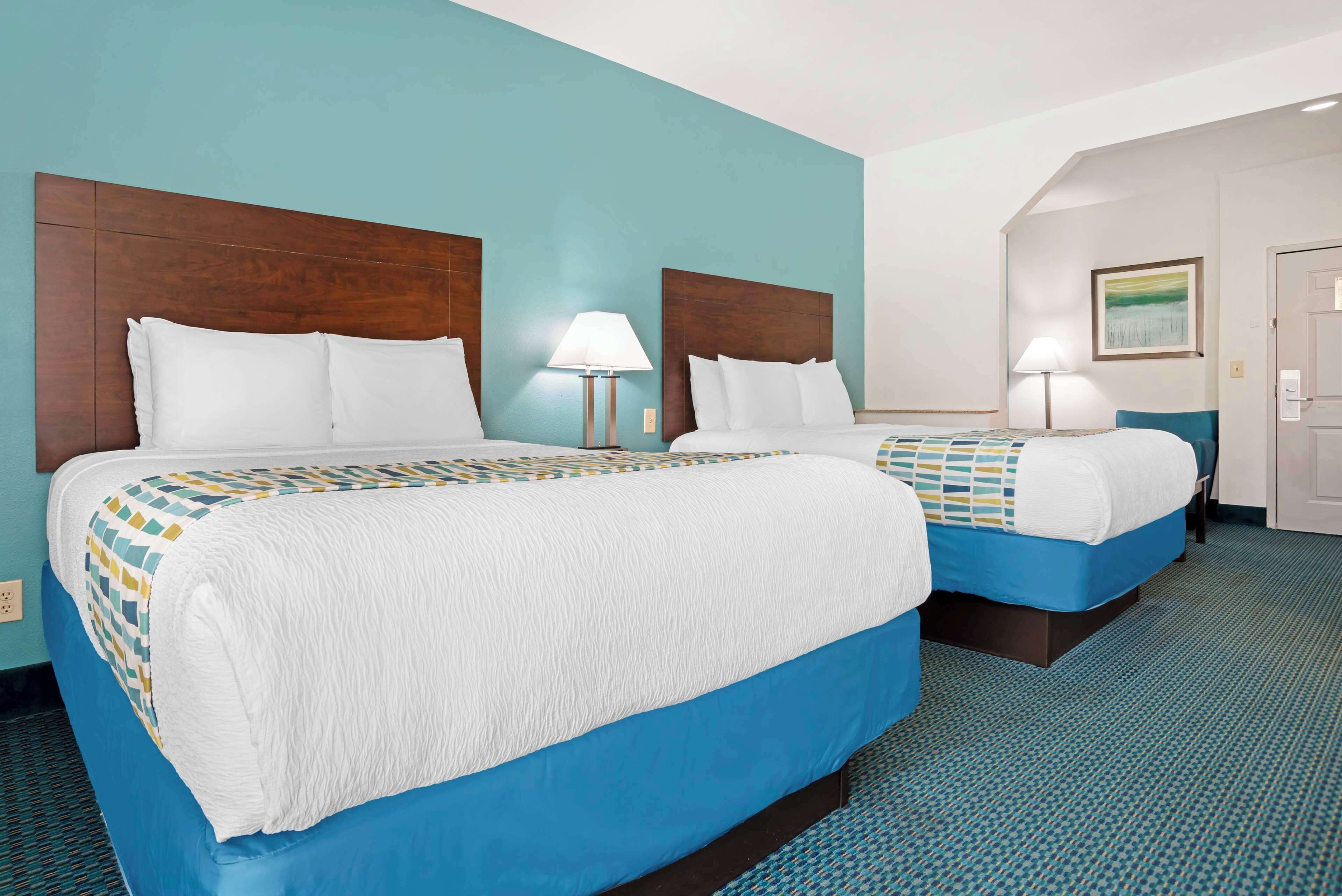 Habitación de hotel con dos camas, una pared color turquesa y una alfombra estampada.