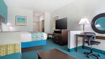 Habitación de hotel con cama, escritorio, silla, televisor y espejo.