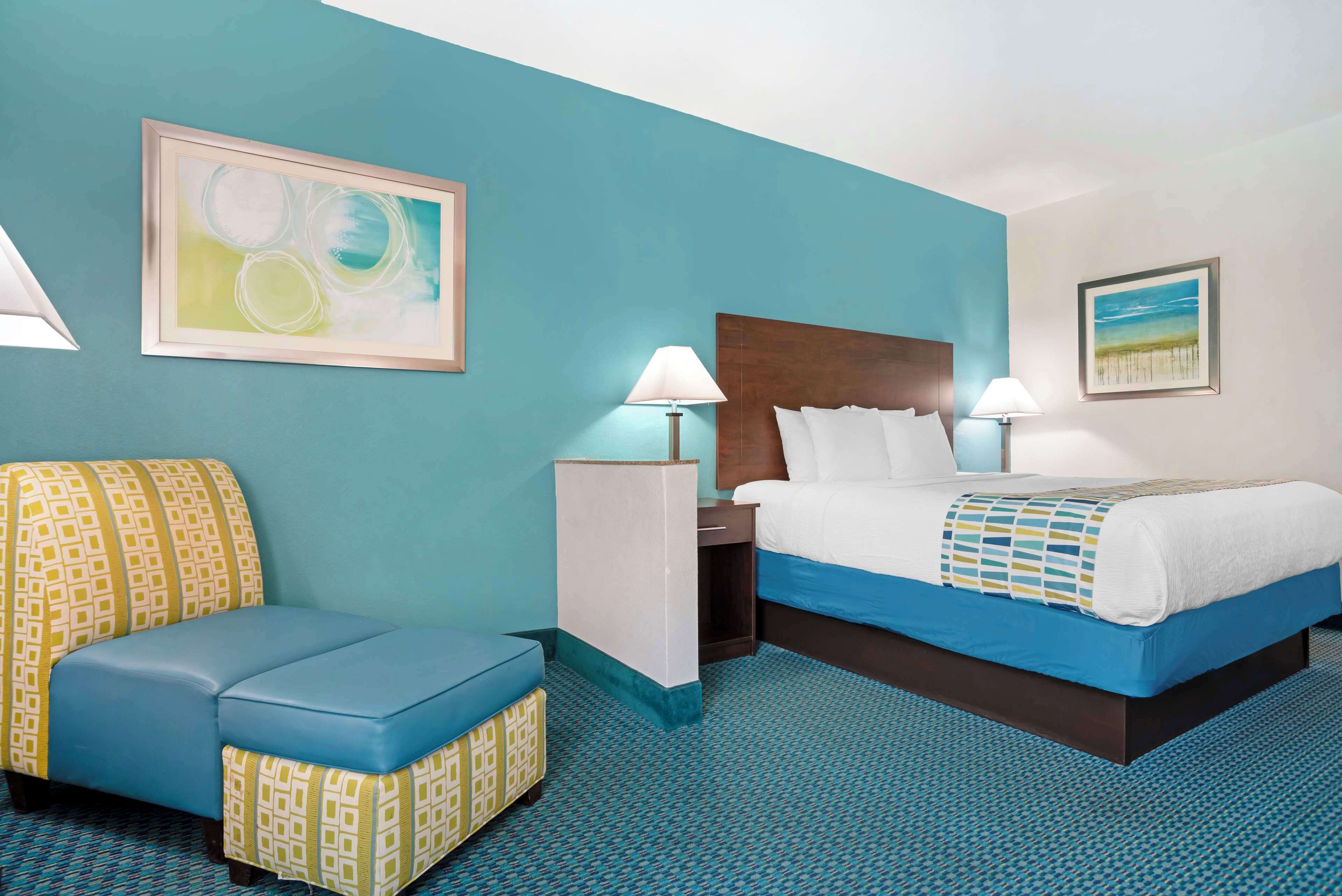 A hotel room with a bed, a sofa, two bedside tables, and a large abstract painting on the wall.