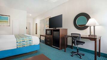 Habitación de hotel con cama, escritorio, silla, televisor, espejo y lámpara.
