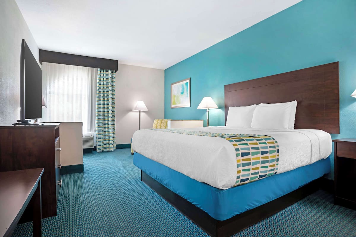 A hotel room with a large bed, a desk, a TV, and a window with curtains.
