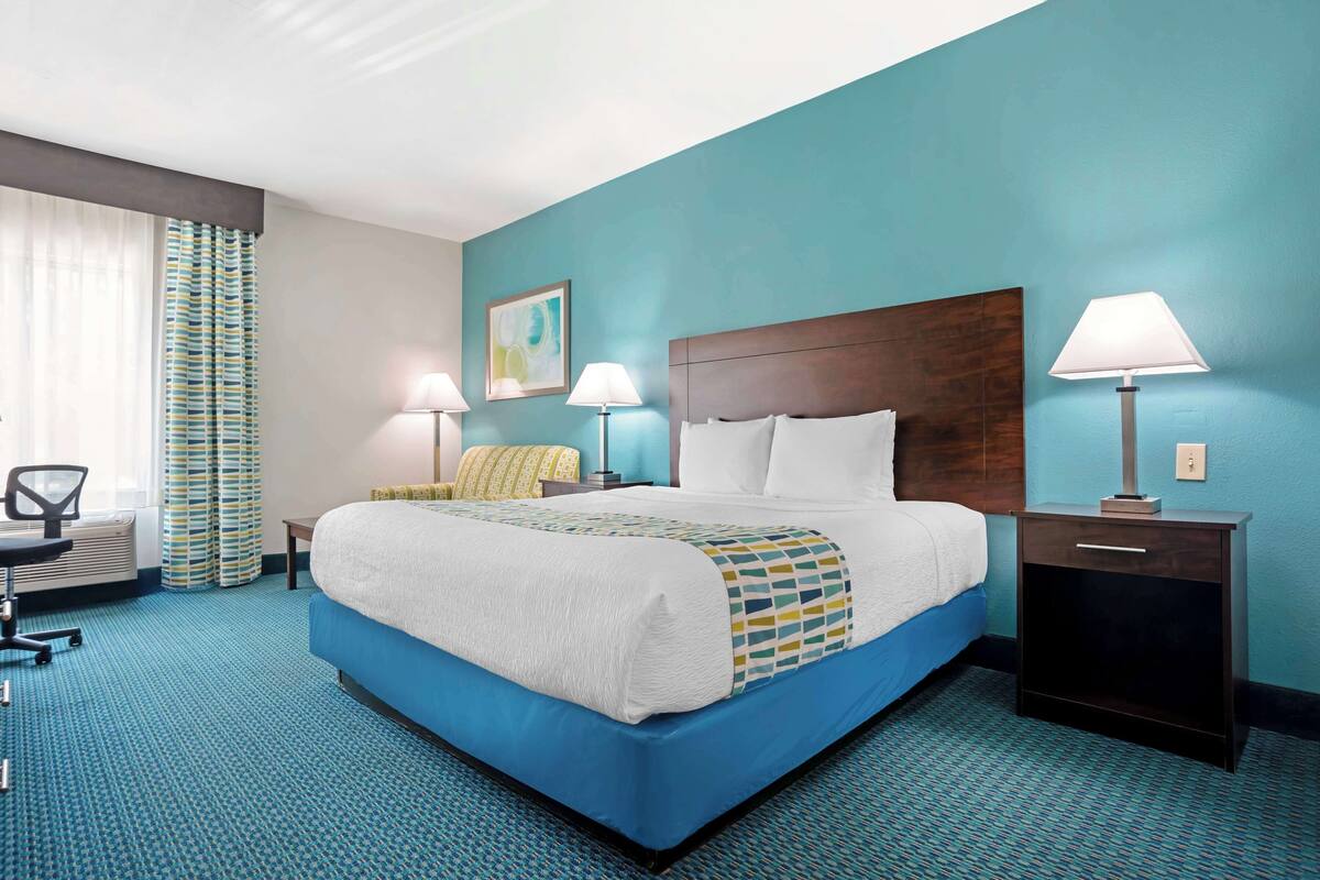 A hotel room with a large bed, two bedside tables with lamps, a chair, and a desk.