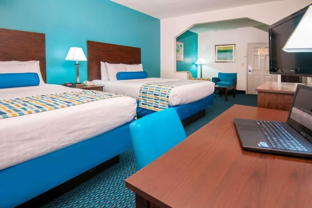 A hotel room with two beds, a desk with a laptop, a TV, and a chair.