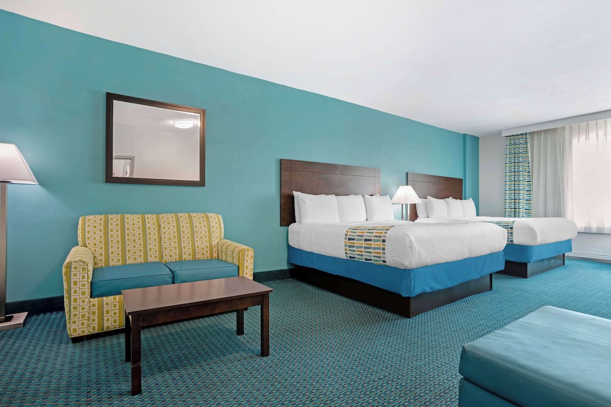 A hotel room with a large bed, a sofa, a small table, and a mirror on the wall.