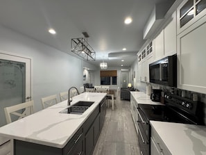 A modern kitchen with a central island, white cabinetry, and a black stove. - St Croix Inn Solon Springs  (Solon Springs)