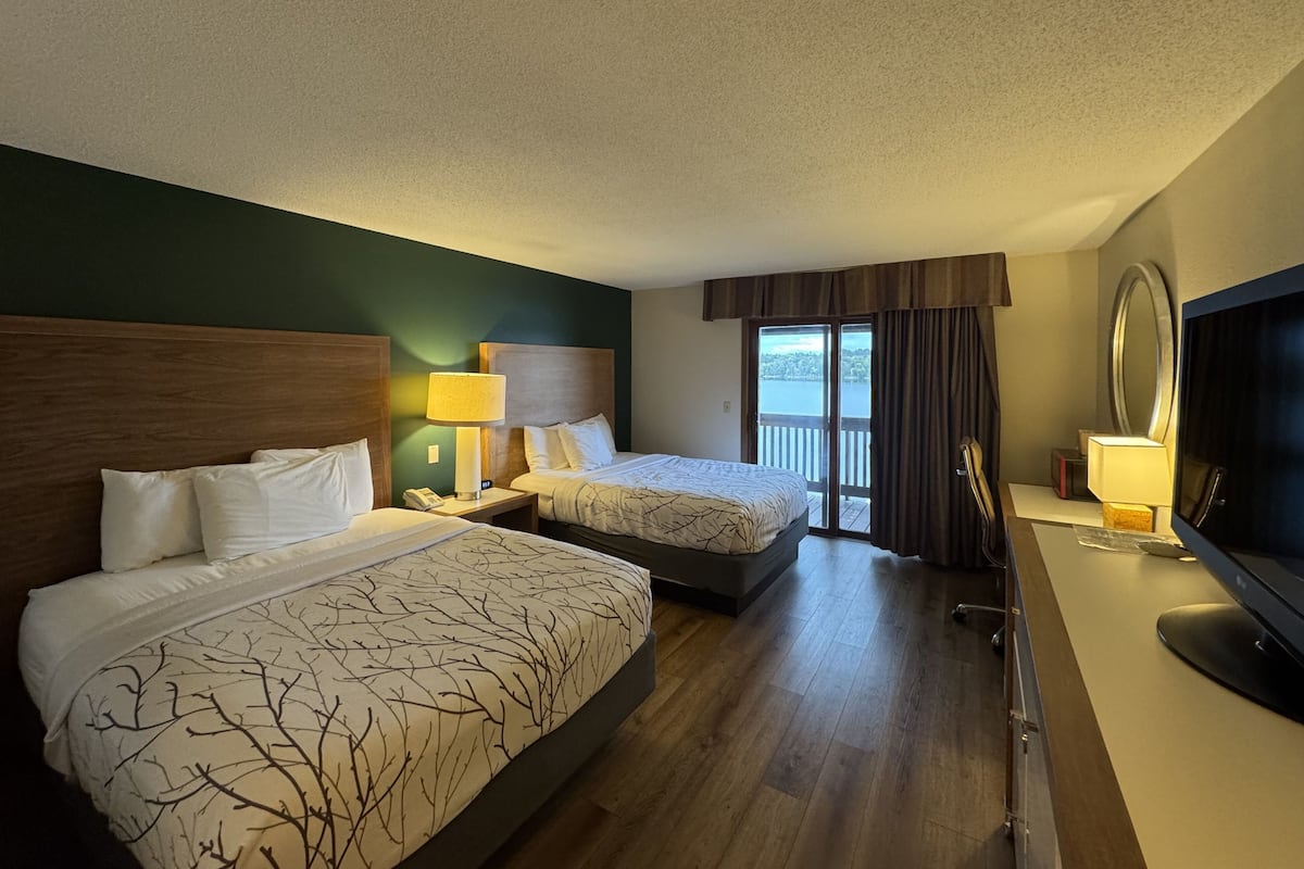 Quarto de hotel com duas camas, uma escrivaninha, televisão e varanda com vista.
