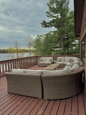 A covered deck with wicker furniture, a wooden table, and a view of a lake and trees. - St Croix Inn Solon Springs  (Solon Springs)
