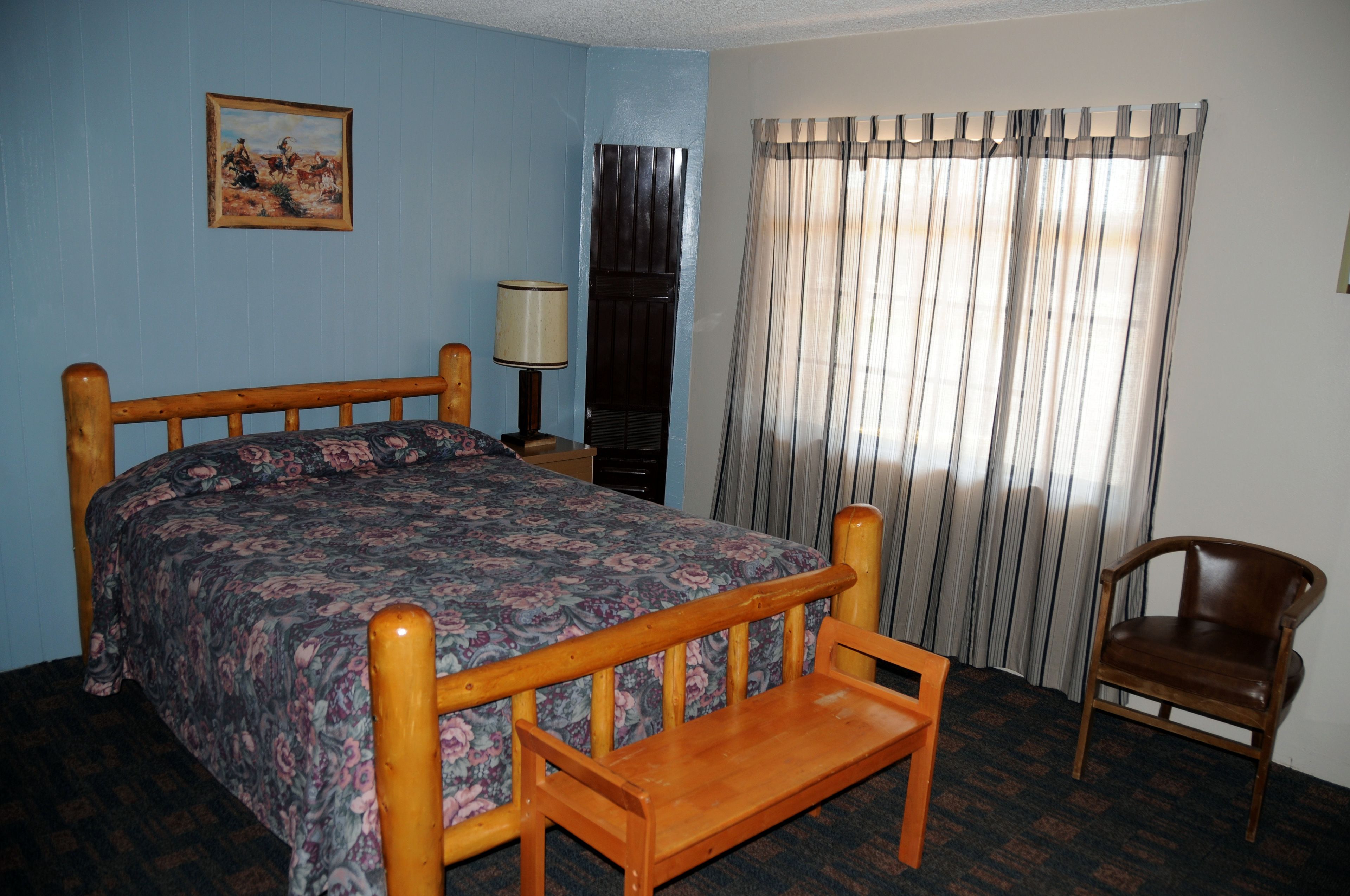 A bedroom with a wooden bed, a chair, a lamp, and a window with curtains.