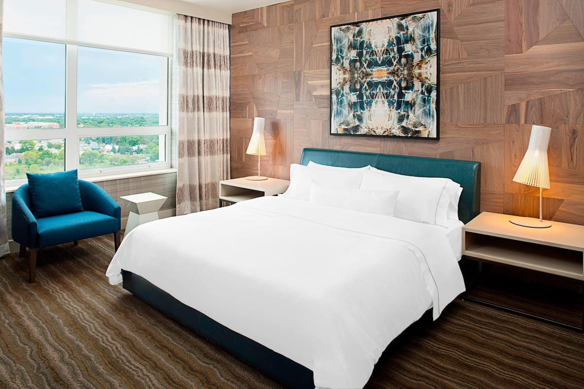 Camera d'hotel con un letto grande, due comodini, una poltrona, una finestra con vista e un quadro astratto appeso alla parete.