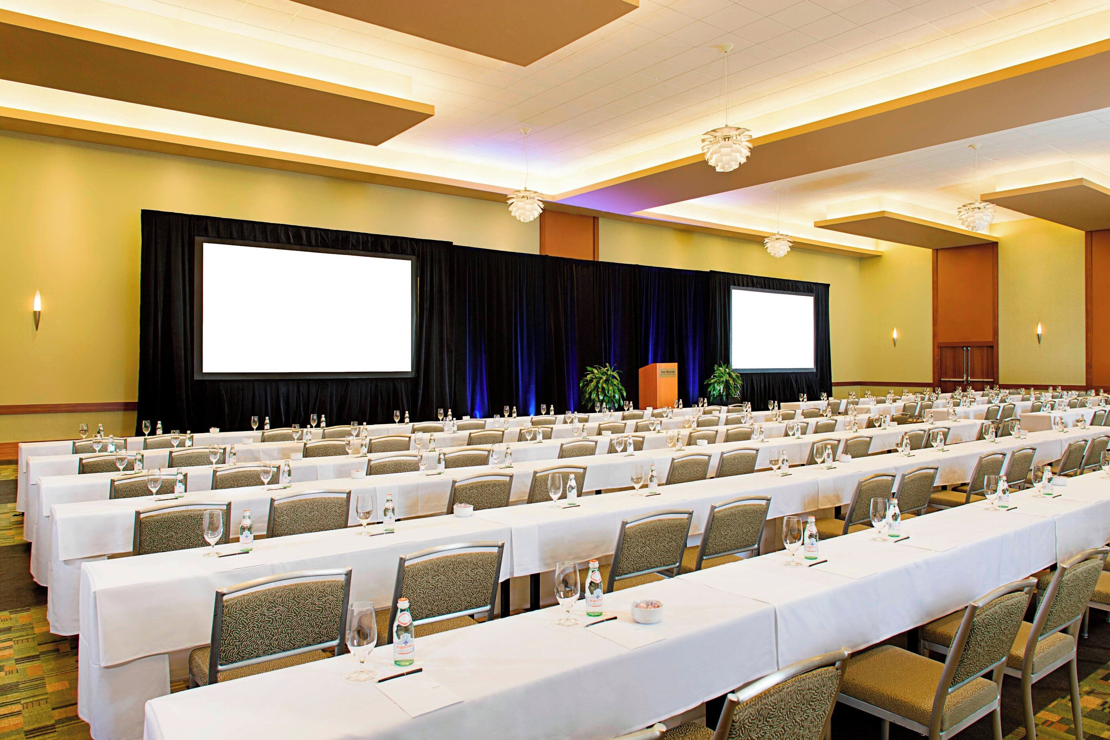 A conference room with long tables, chairs, and a large screen.