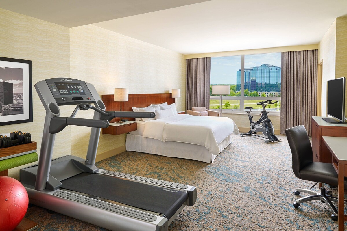 A hotel room with a bed, a desk, a treadmill, and an exercise bike.
