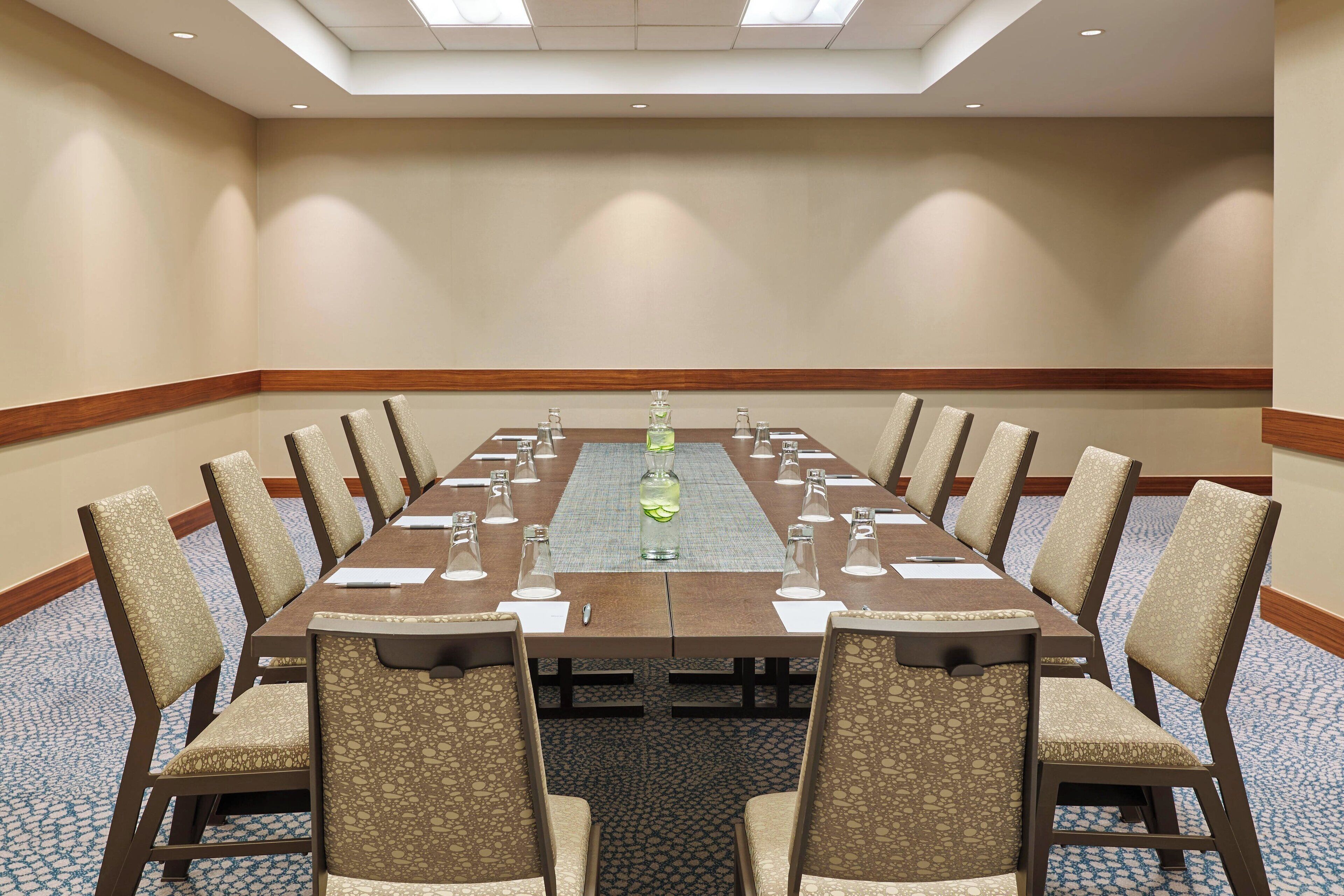 Un salón de conferencias con una larga mesa, sillas y un vaso de agua.