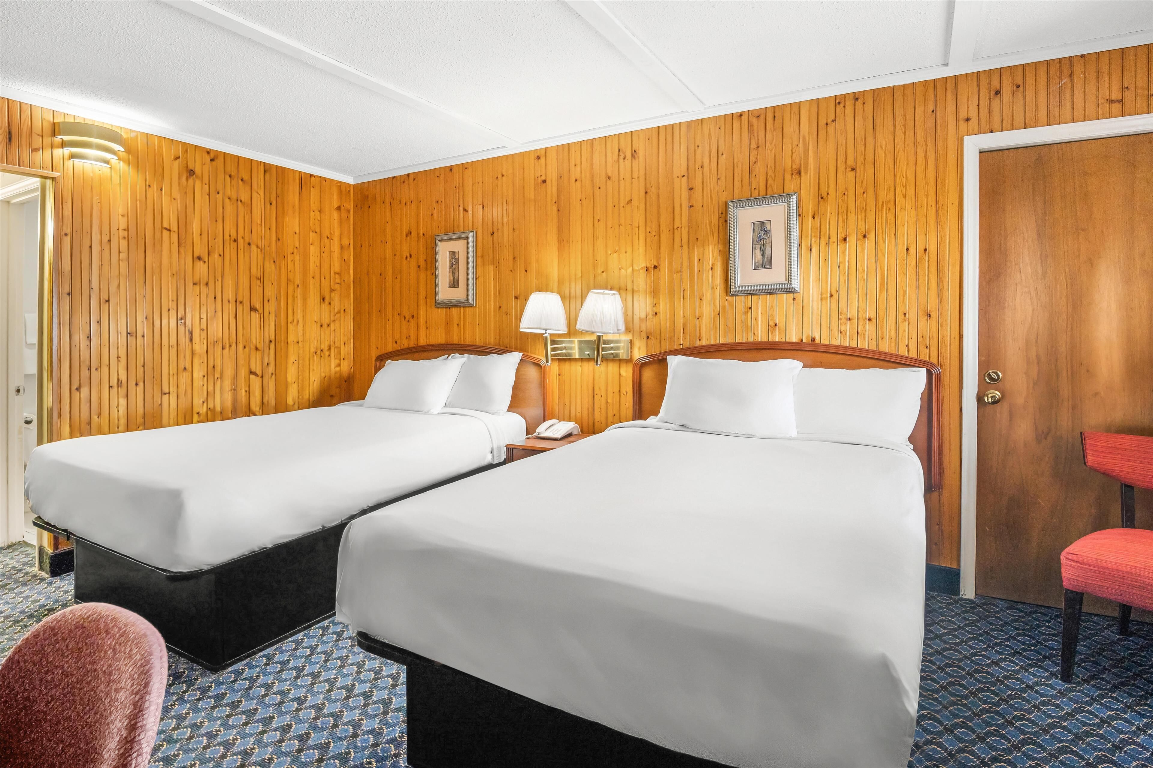 Una habitación de hotel con dos camas, paneles de madera, alfombra estampada y una silla roja.