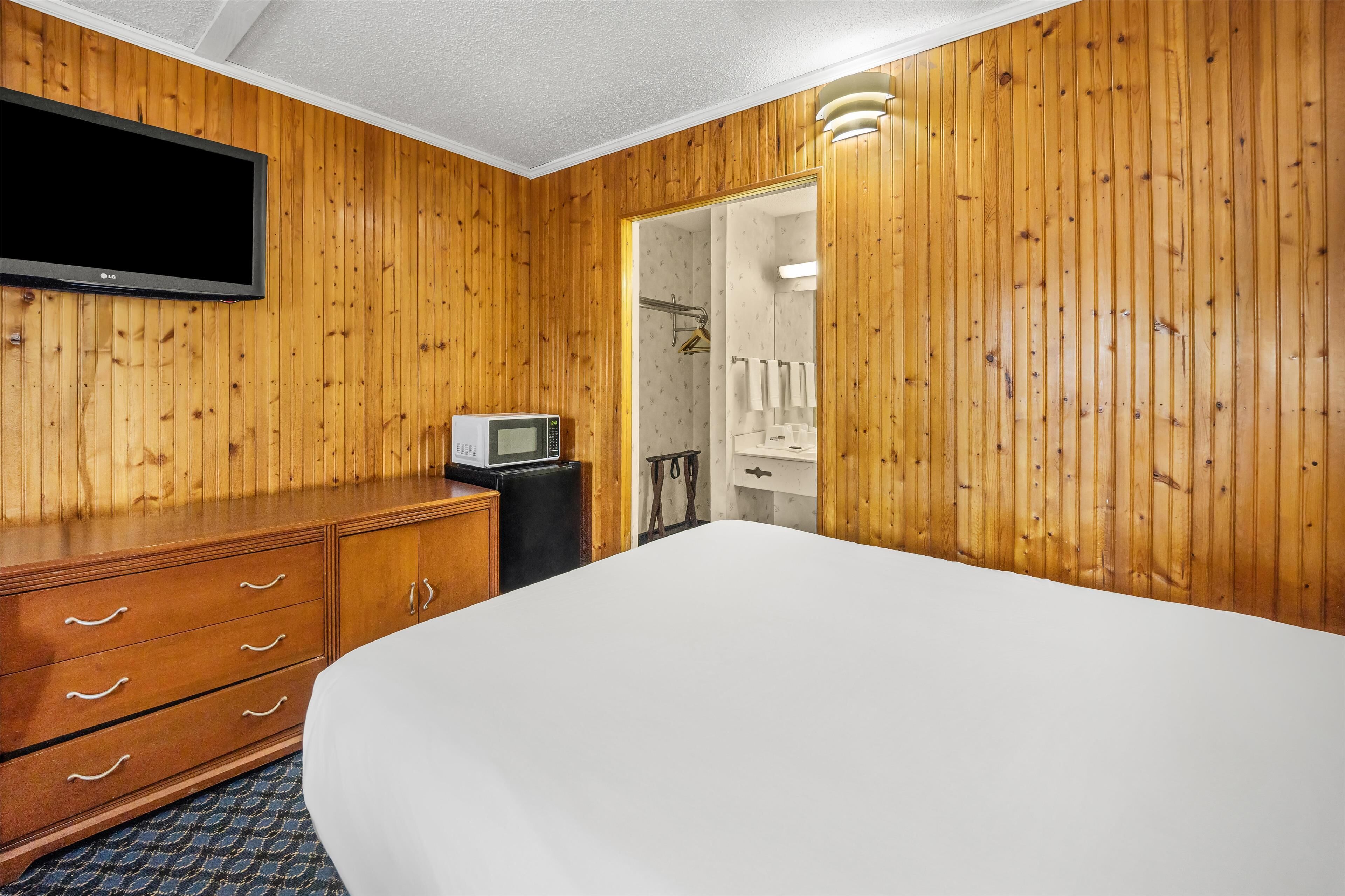 Ein Hotelzimmer mit Holzwandverkleidung, einem Flachbildfernseher, einer Mikrowelle, einer Kommode mit Schubladen und einem großen Bett.