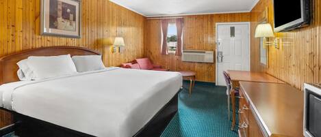 A hotel room with a wooden paneled wall, a bed with white linens, a television, a desk, and a chair.
