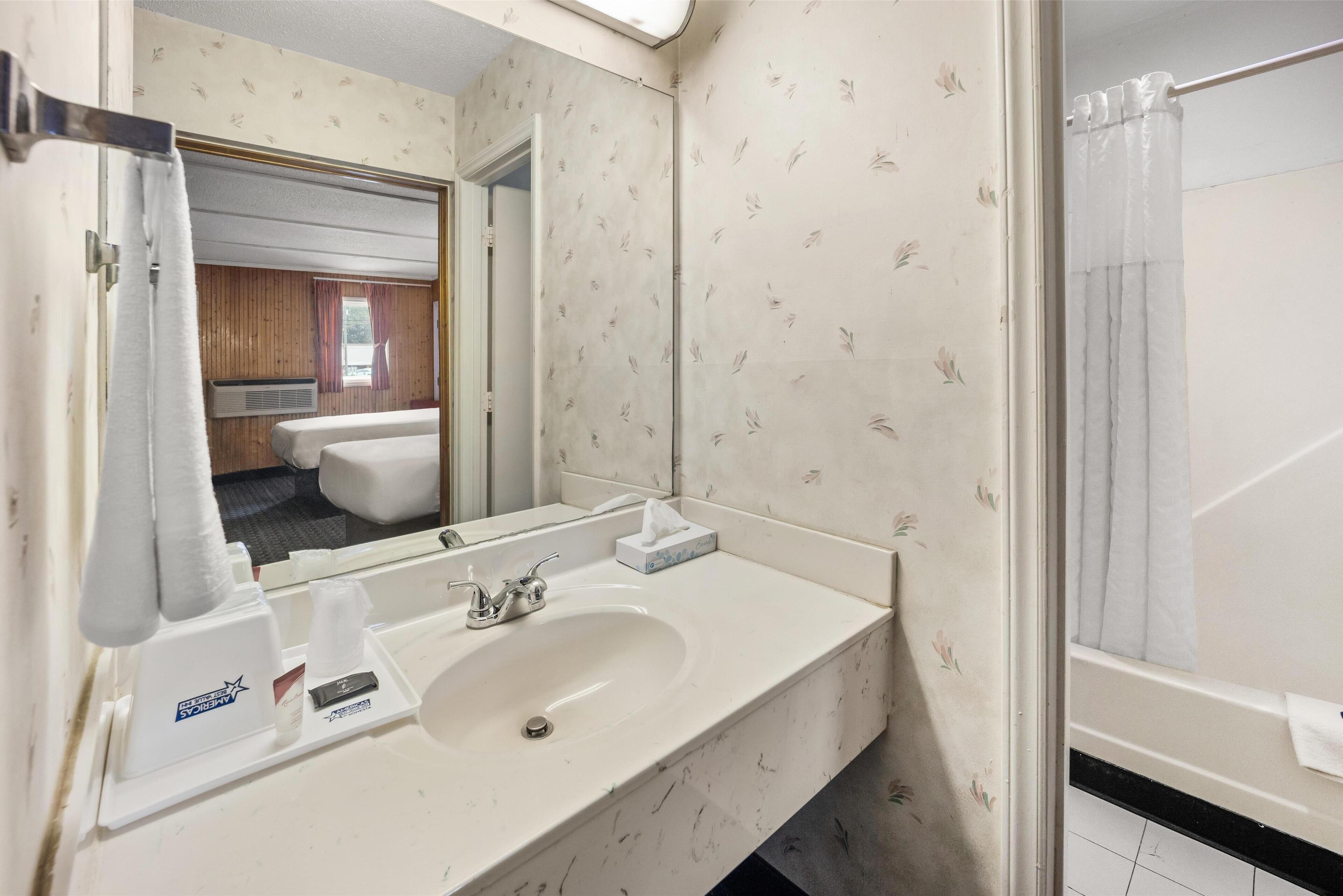 Une salle de bain avec un lavabo blanc, un miroir, un porte-serviettes et un rideau de douche.