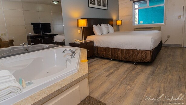 Una camera d'albergo con una grande vasca da bagno, un letto con testiera marrone, due lampade ai comodini e una finestra vista cielo.
