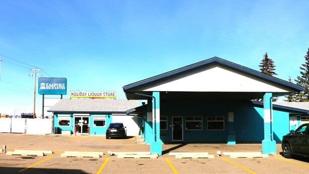 A Holiday Liquor Store with a blue and white building, a car parked in front, and a clear sky. - Empire Inn & Suites (Red Deer)