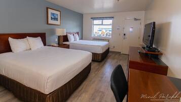 A hotel room with two beds, a desk, a television, and a window with a view of the outside.