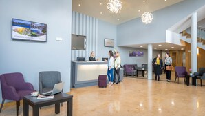 Zona de recepción de un hotel con mostrador, área de descanso y una escalera.