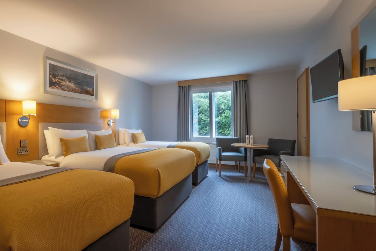 A hotel room with two beds, a desk, a chair, and a window with curtains.
