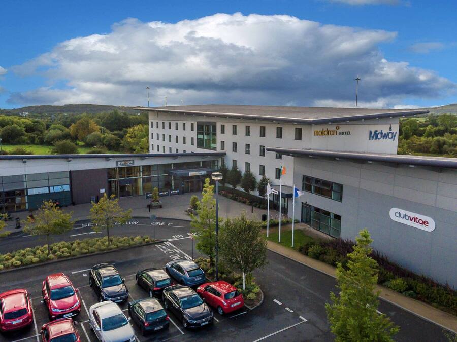Ein Hotel mit modernem Design, das einen großen Parkplatz mit mehreren Autos, eine Grünfläche und einen Blick auf die umliegende Landschaft bietet.