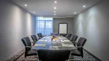 A conference room with a long table, black leather chairs, a projector screen, and a window with blinds.