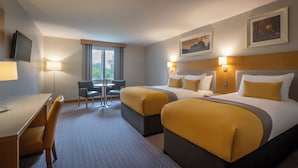 Habitación de hotel con dos camas, un escritorio, una silla y una ventana con cortinas.