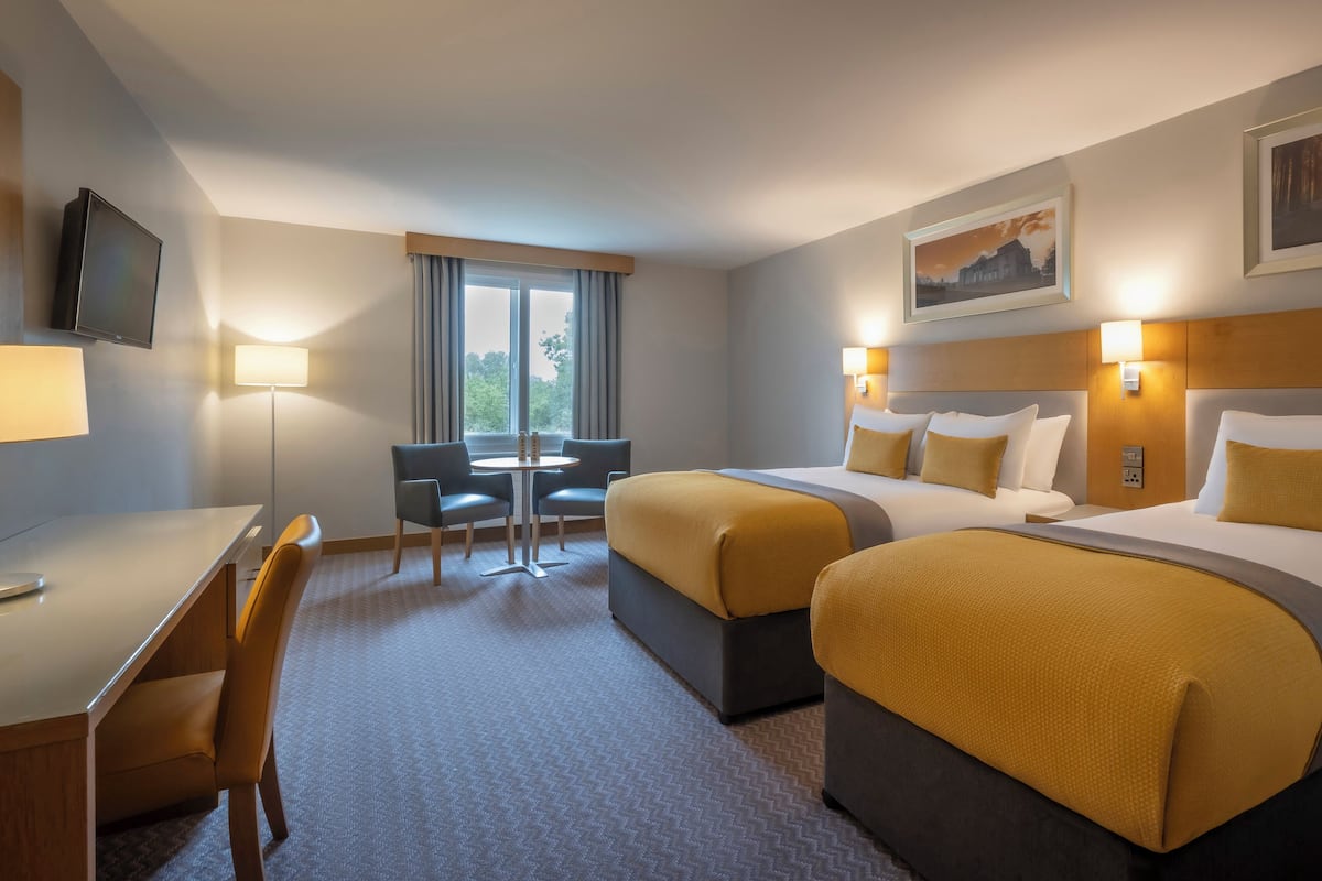 A hotel room with two beds, a desk, a chair, and a window with curtains.