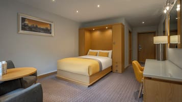Een hotelkamer met een bed, een bureau, een stoel, een spiegel en een schilderij aan de muur.