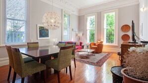 Un espace repas avec une table et des chaises en bois, un lustre et une vue sur la verdure environnante.