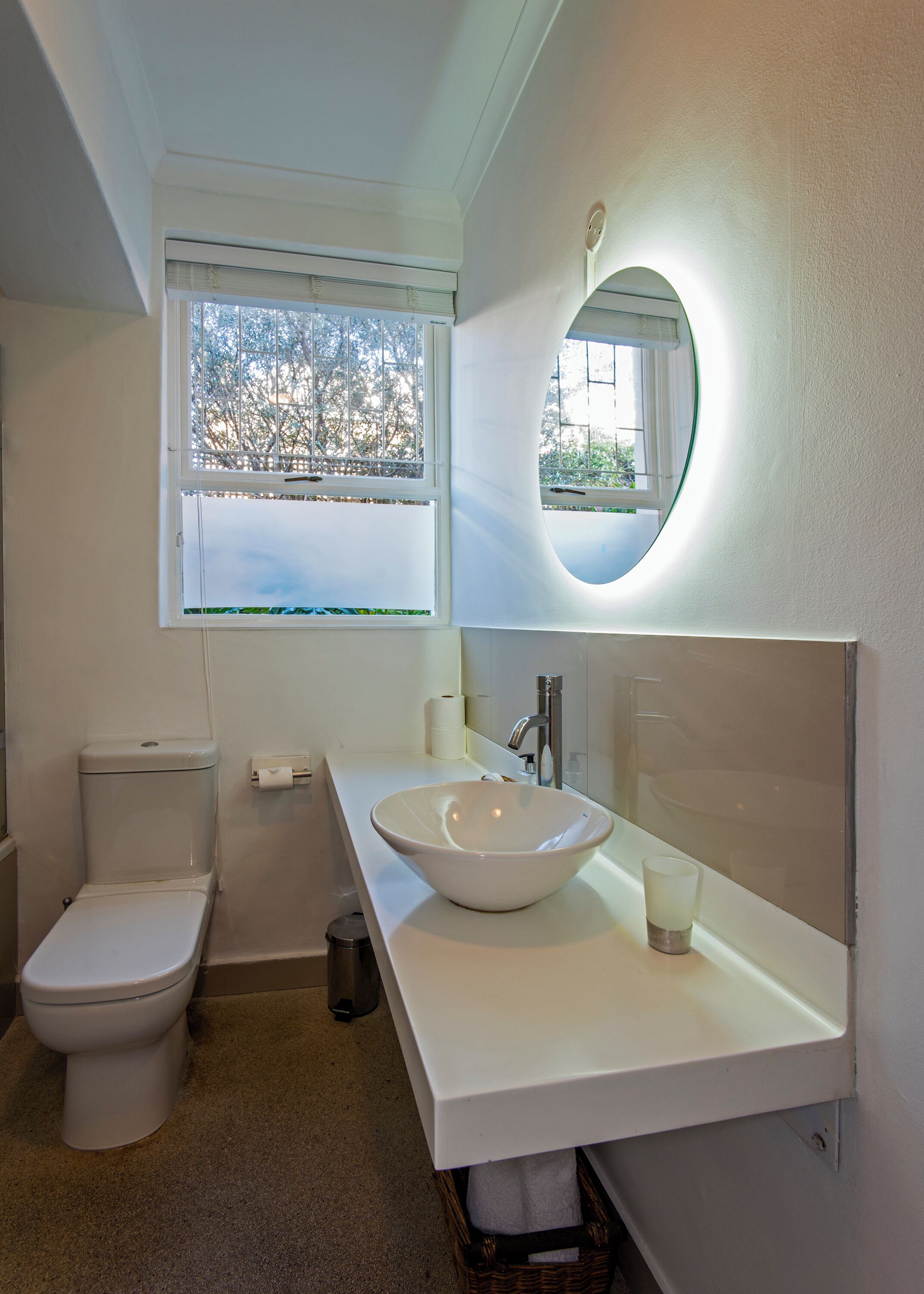 A modern bathroom with a white sink, a toilet, and a window with a view of trees.