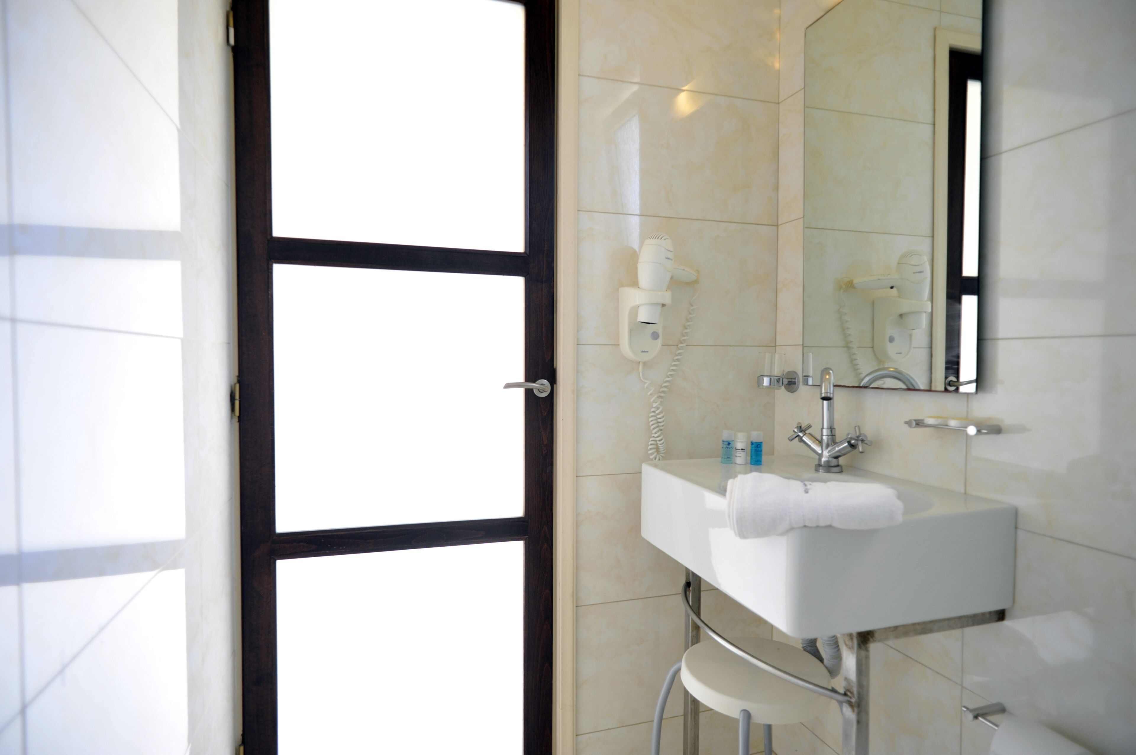 Une salle de bain avec un lavabo blanc, un miroir et un sèche-cheveux fixé au mur.