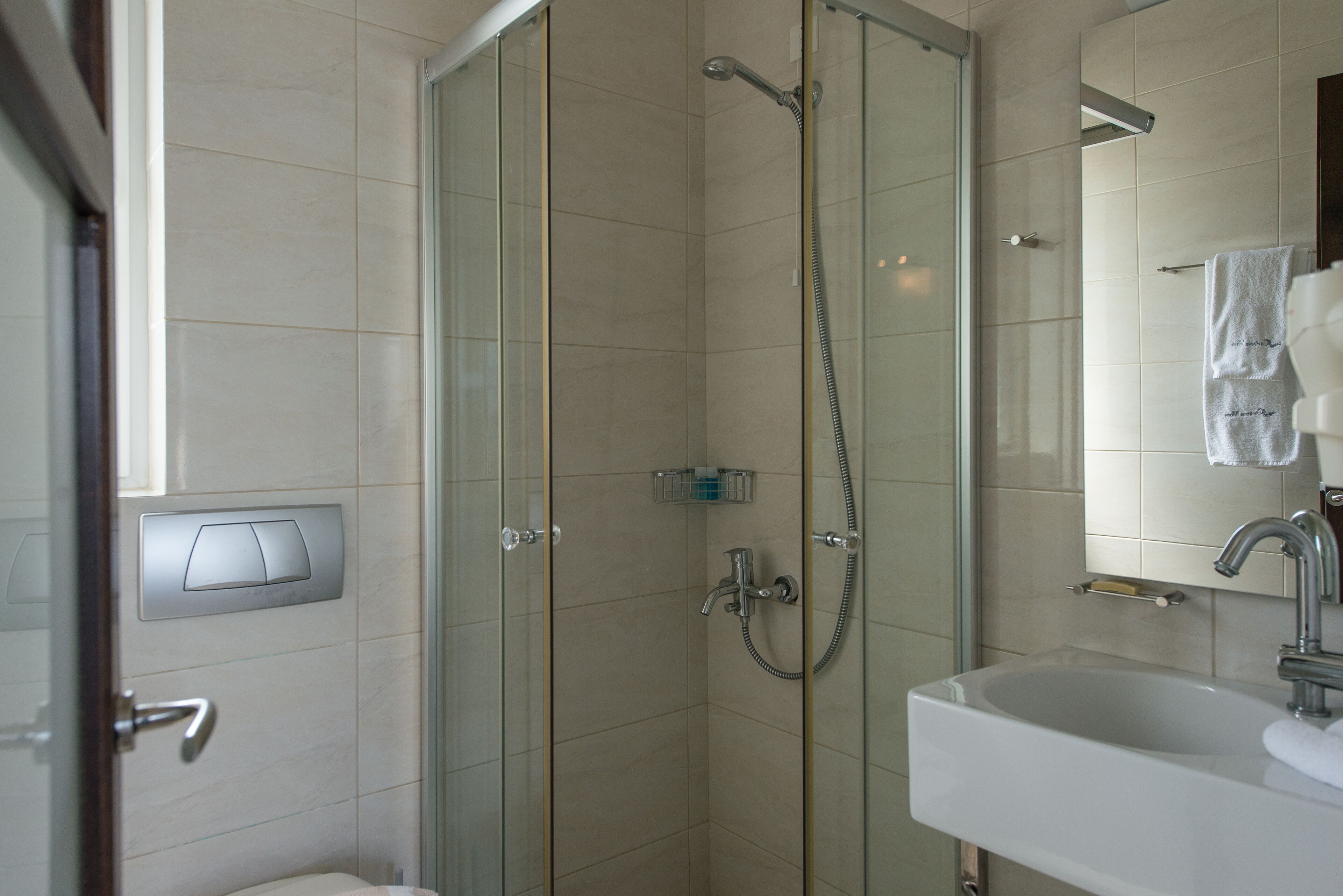 A modern bathroom with a glass-enclosed shower, a white sink, and a towel hanging on the wall.