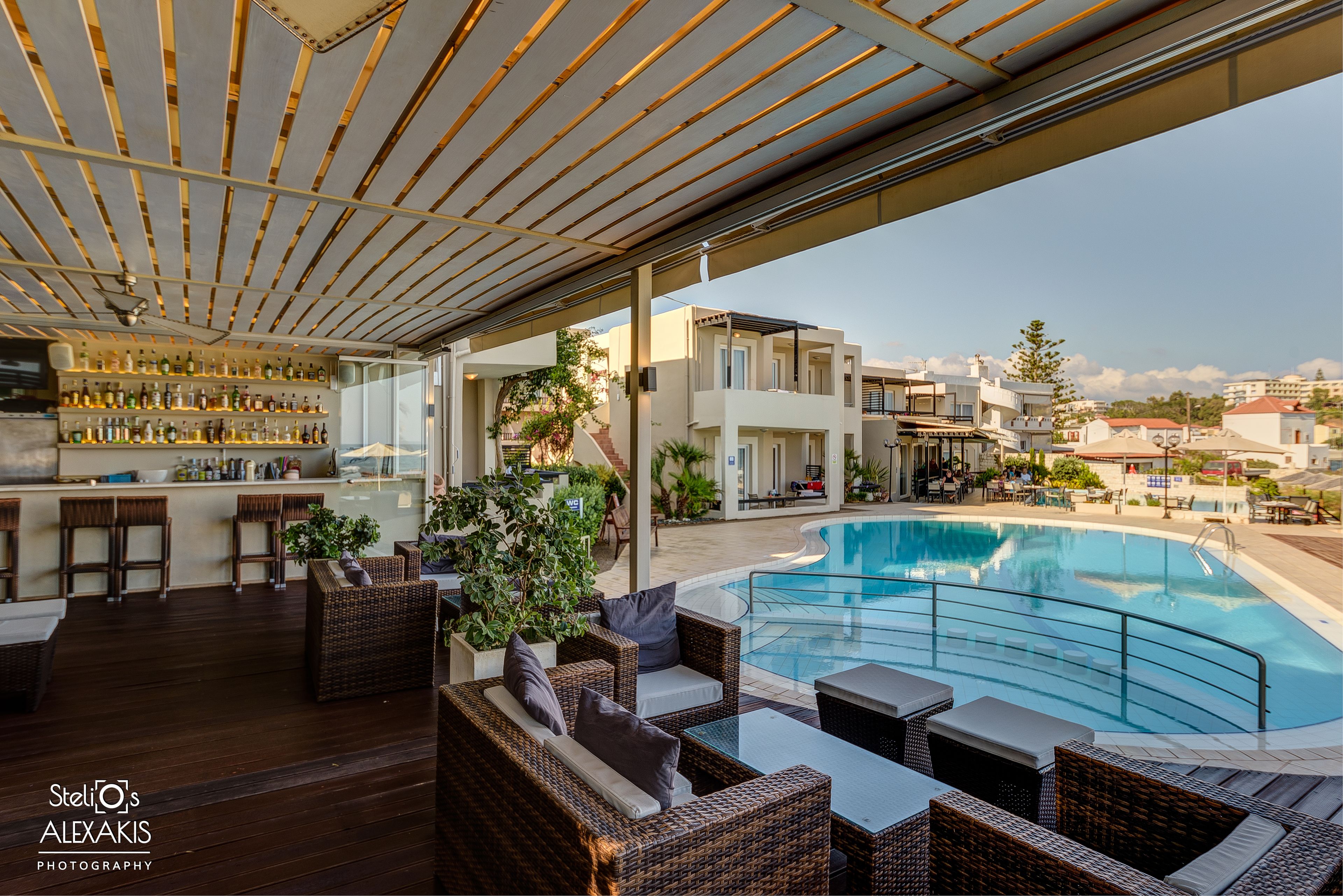 Un bar en la azotea con mobiliario de mimbre, una piscina y vistas de la ciudad.