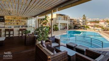 Un bar en la azotea con mobiliario de mimbre, una piscina y vistas de la ciudad.