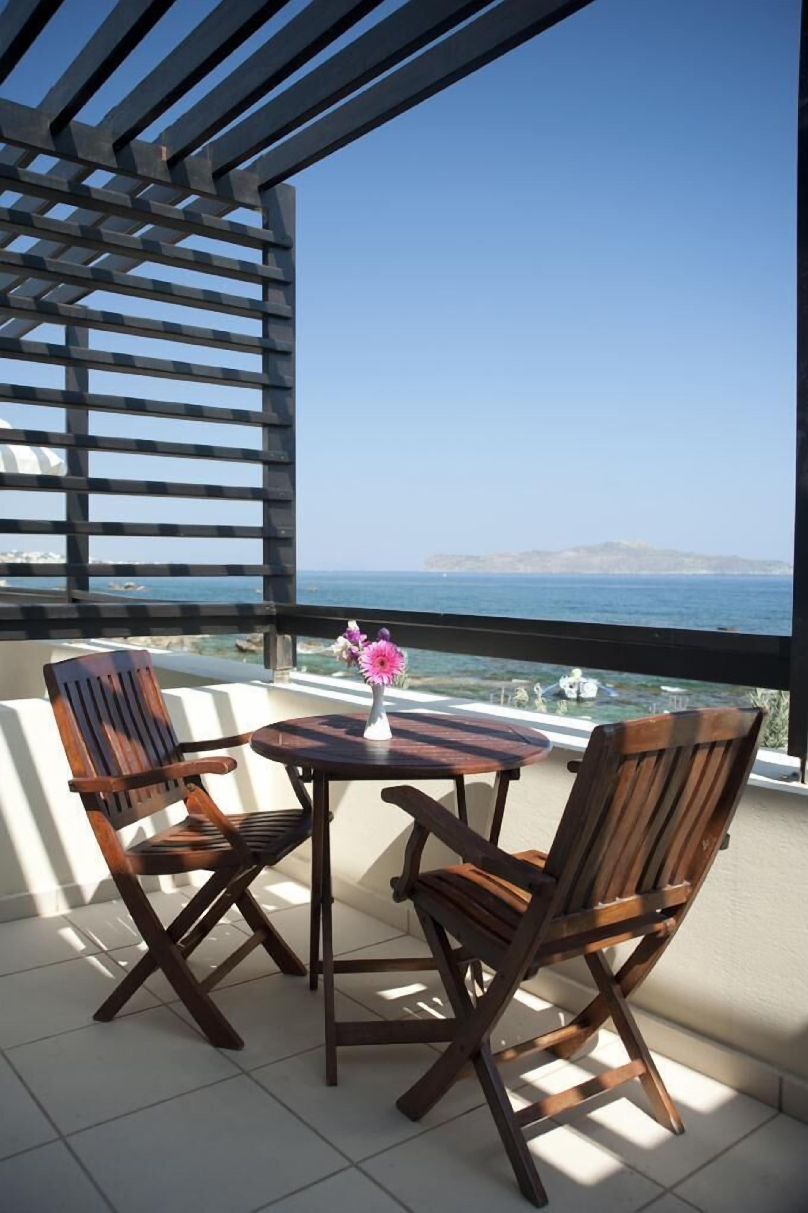 Een balkon met twee houten stoelen en een tafeltje, met uitzicht op de kust.