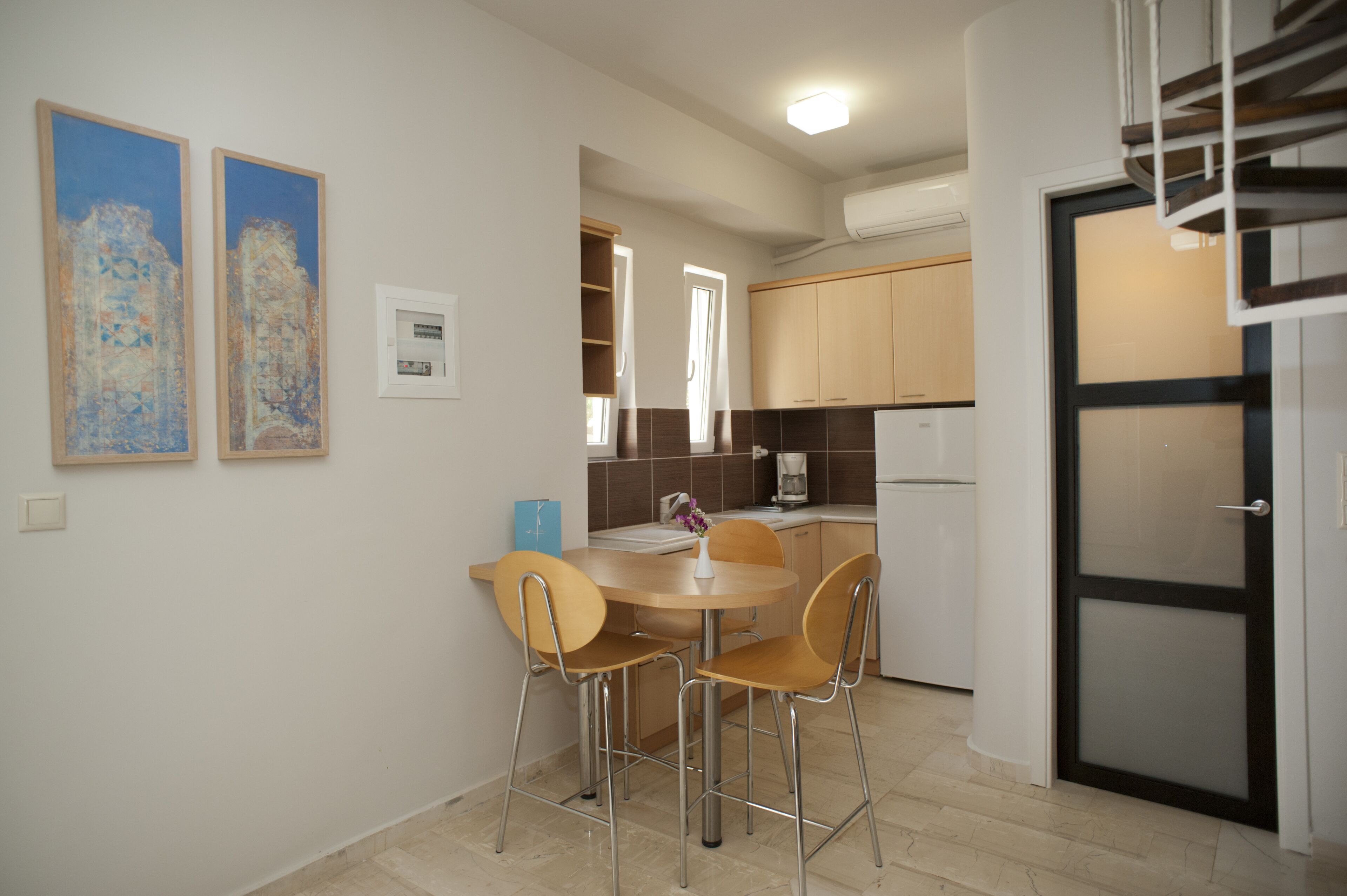 A modern kitchen with a dining area, featuring a round table, chairs, and artwork on the wall.