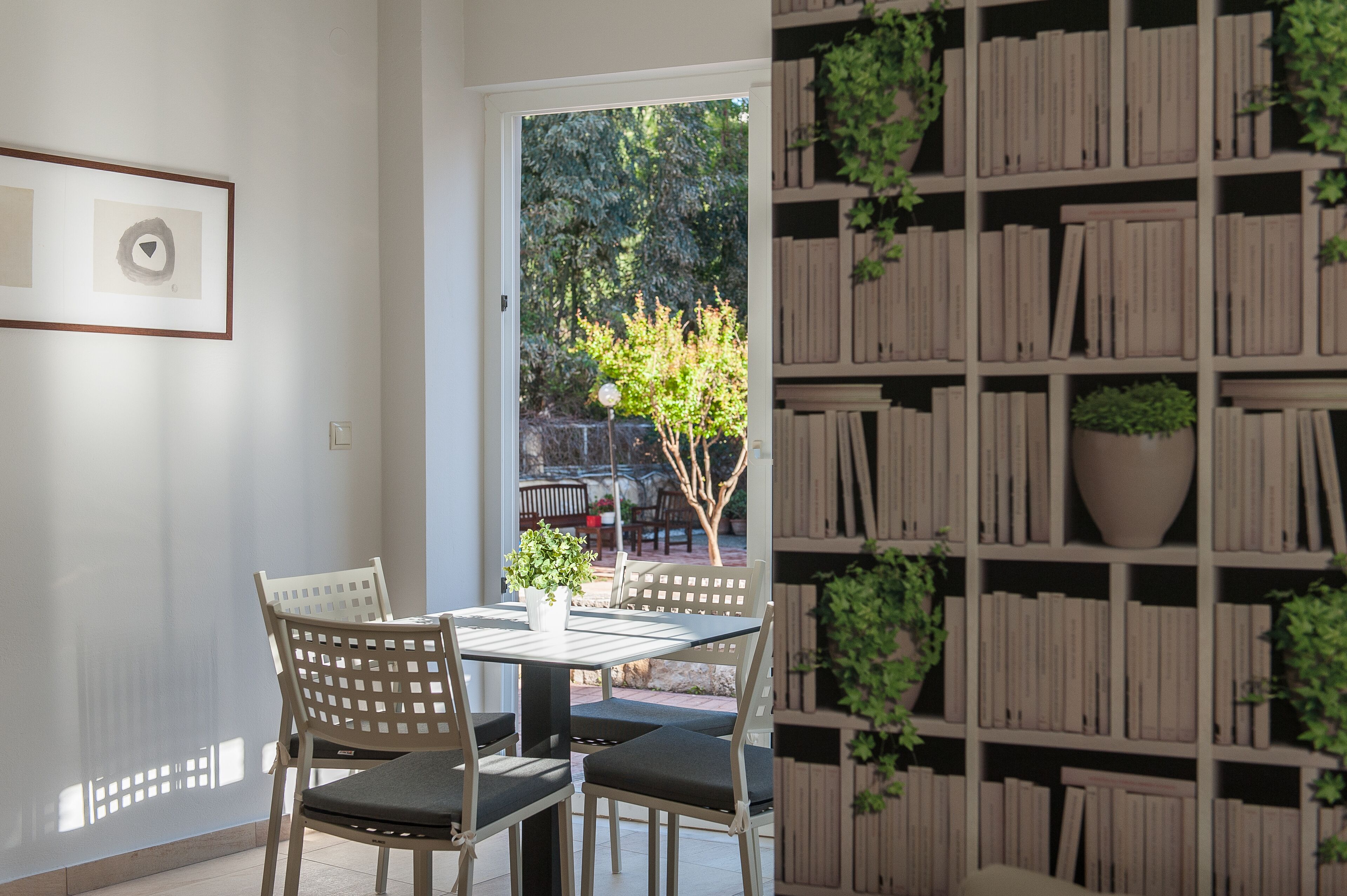 A room with a dining table and chairs, a bookshelf, and a door leading to an outdoor area with a tree and patio furniture.